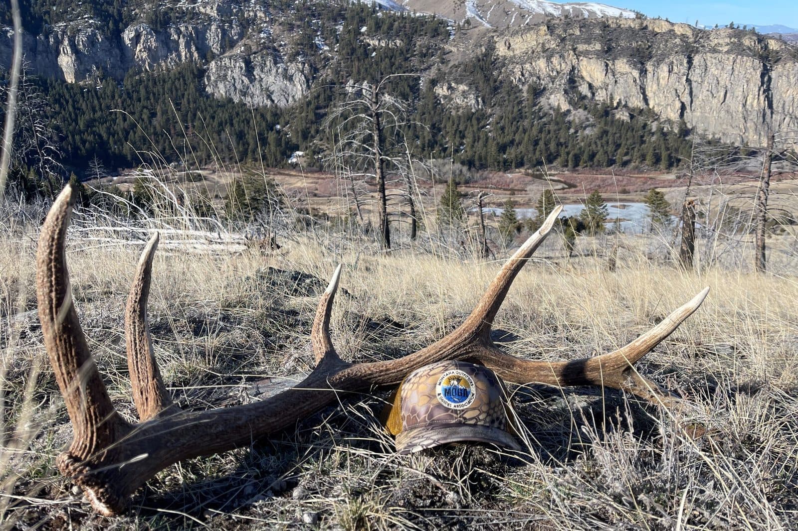 A MOGA cap resting on a shed elk antler above a Montana river valley